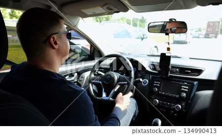 Confident man in sunglasses looking concentrated to urban road while riding automobile. Serious male driver driving a motor car at town. Guy operating the auto at highway. Slow motion 134990413