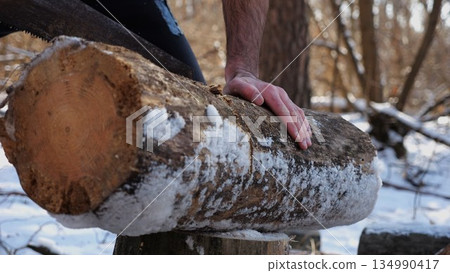 Male hand sawing a log in sunny winter forest. Strong guy working with a saw in snowy woodland. Concept of strength, masculine, energy, and harmony with nature during cold season. Slow motion 134990417