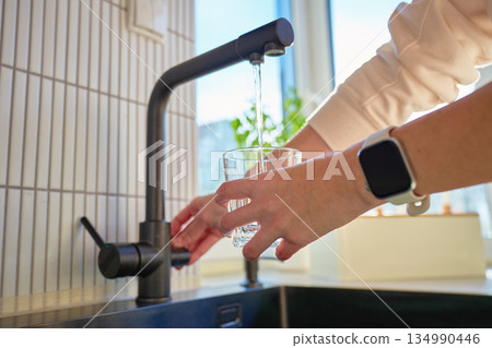 Hand filling glass with drinking water from kitchen faucet Hand filling glass with drinking water from kitchen faucet 134990446