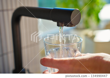Glass filled with clear water from black kitchen faucet in daylight Glass filled with clear water from black kitchen faucet in daylight 134990447