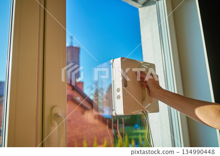 Woman starting robotic window cleaner on glass surface of window 134990448