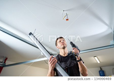 Electrician holding lamp and drill preparing ceiling lighting installation Electrician holding lamp and drill preparing ceiling lighting installation 134990469