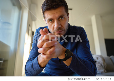Worried man looking at camera with clasped hands sitting indoors 134990483