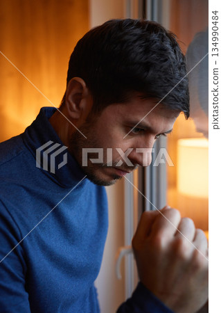 Worried man leaning on window at home Worried man leaning on window at home 134990484
