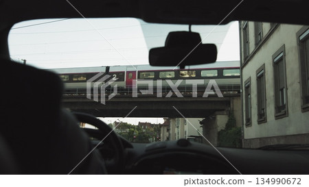 A man rides in a car at sunset on the streets of a modern city. The navigator is included. Shooting from the back seat. Passes under the bridge and the train goes from above. A man rides in a car at sunset on the streets of a modern city. The navigator is included. Shooting from the back seat. Passes under the bridge and the train goes from above. 134990672