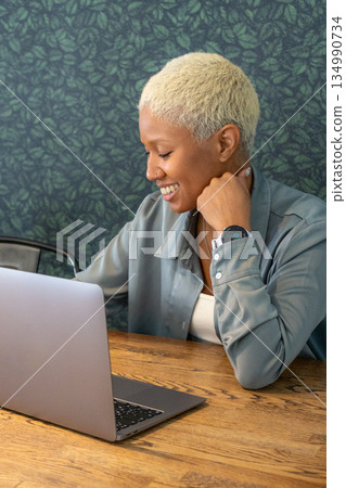 African-American woman with short blond hair is sitting at desk with laptop in front of her. African-American woman with short blond hair is sitting at desk with laptop in front of her. 134990734