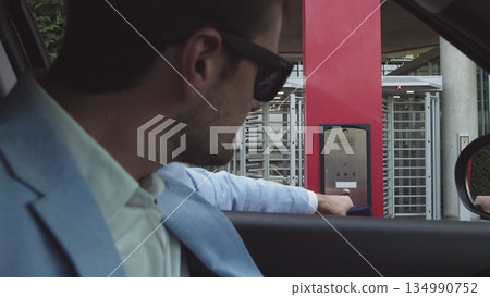 young male businessman in nice suit and glasses paying for parking by bank card with car leaving his office. Office and parking security. 134990752