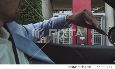 young male businessman in nice suit and glasses paying for parking by bank card with car leaving his office. Office and parking security. young male businessman in nice suit and glasses paying for parking by bank card with car leaving his office. Office and parking security. 134990755