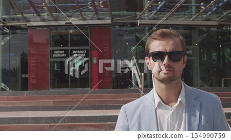 Good-looking confident purposeful adult bearded businessman in glasses in stylish suit going down on steps while leaving the office building and looking at camera. Good-looking confident purposeful adult bearded businessman in glasses in stylish suit going down on steps while leaving the office building and looking at camera. 134990759