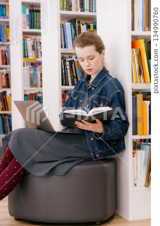 woman sits at shelves in library and reads book. education, scientific work. business person. woman sits at shelves in library and reads book. education, scientific work. business person. 134990760