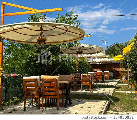 Outdoor cafe garden with wooden tables and umbrellas. Summer dining space, relaxed atmosphere, hospitality and open air leisure 134990831