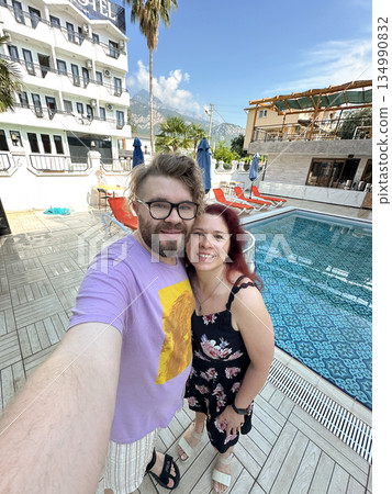 Couple taking selfie near hotel swimming pool outdoors. Vacation mood, travel lifestyle, summer leisure and joyful relationship moment 134990832