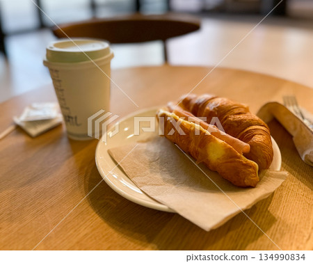 Croissant sandwich with ham and coffee on cafe table. Simple breakfast, casual dining, warm atmosphere and everyday food routine Croissant sandwich with ham and coffee on cafe table. Simple breakfast, casual dining, warm atmosphere and everyday food routine 134990834