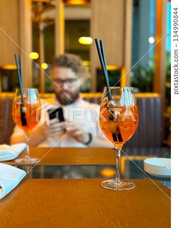 Aperitif cocktails with ice and straws on restaurant table. Modern dining, evening leisure, social connection, slow lifestyle and relaxed urban atmosphere 134990844