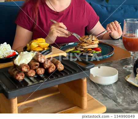 Woman enjoying a restaurant meal with grilled meat and side dishes. Casual dining, comfort food Woman enjoying a restaurant meal with grilled meat and side dishes. Casual dining, comfort food 134990849