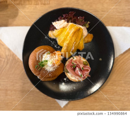 Assorted appetizers arranged on a black plate on a wooden table. Casual dining, tasting experience, comfort food, culinary variety, cafe culture, relaxed atmosphere, and enjoyment of small portions 134990864