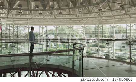 Side view of a thoughtful businessman in a suit walking in his office, contemplating the next big business deal, looking ahead. Casual office in the middle Side view of a thoughtful businessman in a suit walking in his office, contemplating the next big business deal, looking ahead. Casual office in the middle 134990905