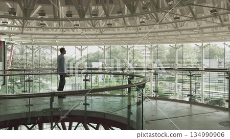 Side view of a thoughtful businessman in a suit walking in his office, contemplating the next big business deal, looking ahead. Casual office in the middle Side view of a thoughtful businessman in a suit walking in his office, contemplating the next big business deal, looking ahead. Casual office in the middle 134990906