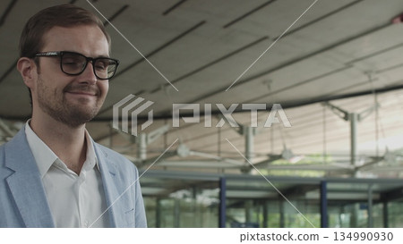 A young businessman, an employee of a large company walks around a modern beautiful office and greets, waves his hand. Shooting with hands close up. The concept of a successful employee 134990930