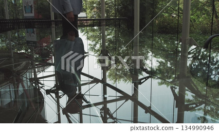 A young handsome man in an architect or lawyer suit walks around a modern office. Reflection in a glass table A young handsome man in an architect or lawyer suit walks around a modern office. Reflection in a glass table 134990946