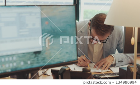 Serious young businessman checking corporate paperwork correspondence sitting at home office desk. Male entrepreneur reading documents, analyzing financial papers, preparing audit report at workplace Serious young businessman checking corporate paperwork correspondence sitting at home office desk. Male entrepreneur reading documents, analyzing financial papers, preparing audit report at workplace 134990994