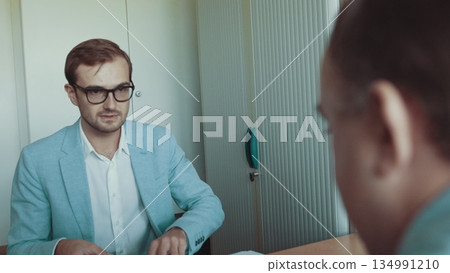 Young handsome man with glasses. A successful employee works with documents. The man sits in office with the director and shows documents. Business conversation in the office. Team of Industrial 134991210