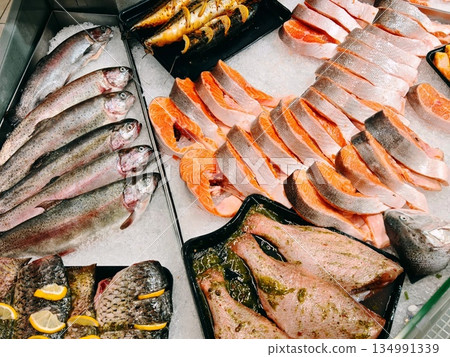Fresh Fish Counter Display. Whole trout and sliced salmon arranged on crushed ice at supermarket fish counter with various prepared seafood portions. 134991339