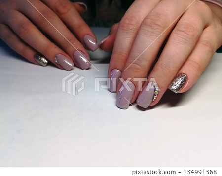 Purple Glitter Accent Manicure. Hands displaying manicured nails in lavender shades with silver glitter accents, rhinestones and glossy top coat on white background. Purple Glitter Accent Manicure. Hands displaying manicured nails in lavender shades with silver glitter accents, rhinestones and glossy top coat on white background. 134991368