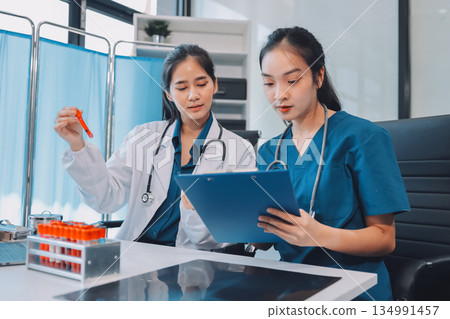 Medical team meeting analyzing blood test results in hospital laboratory. Doctors and scientists in lab coats are having a discussion about blood test result, holding test tubes and taking notes. 134991457