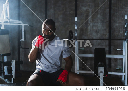 Fitness workout in gym. African man fighter preparing for fight punching with red boxing wraps sports protective bandages in gym. Strong man training punches ready for fight boxing sparring training 134991918