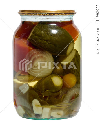 Glass jar with pickled whole cucumbers, red tomatoes, half an onion and garlic cloves in clear brine 134992065