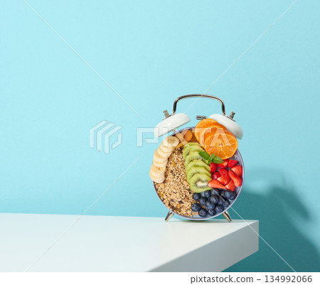 A creative breakfast in the shape of an alarm clock with fruits and cereals on a blue background. 134992066