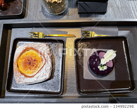 Two black plates with cream puff and luxury purple desserts Two black plates with cream puff and luxury purple desserts 134992298