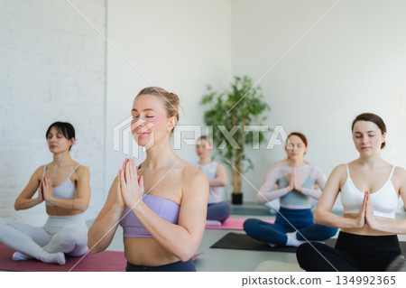 Yoga mindfulness meditation. Group of sporty people doing exercise in studio for class for yoga wellness mindfulness meditation. Men women practicing yoga sitting in lotus pose meditating relaxing Yoga mindfulness meditation. Group of sporty people doing exercise in studio for class for yoga wellness mindfulness meditation. Men women practicing yoga sitting in lotus pose meditating relaxing 134992365