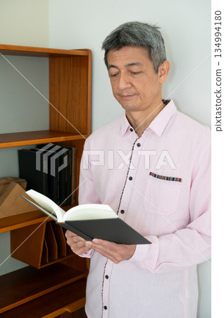 A man reading a book in front of a bookshelf A man reading a book in front of a bookshelf 134994180