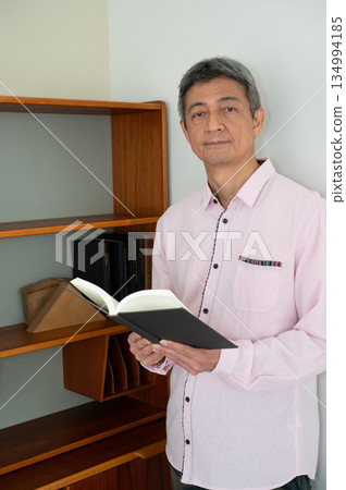 A man reading a book in front of a bookshelf A man reading a book in front of a bookshelf 134994185