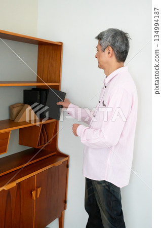 A man picking up a book from a bookshelf A man picking up a book from a bookshelf 134994187
