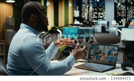 African american worker attending a remote web call at desk using webcam on laptop, interacting with stakeholders after hours. Executive assistant exchanging ideas for networking session. 134994973