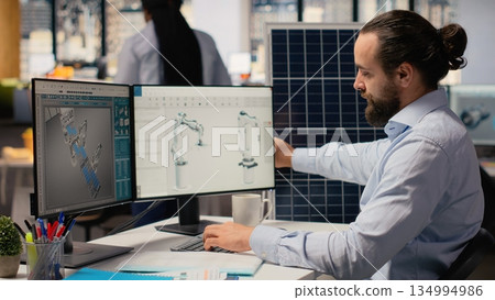 Sustainability RD expert uses CAD program on PC to design production lines for solar panel assembly. Worker runs simulation tools to enhance solar cells, accelerating clean energy adoption, camera B 134994986