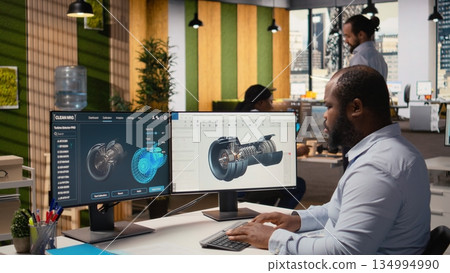 Engineer in office working on wind turbine component CAD design, doing eco friendly energy research. Employee doing digital modeling of wind energy generator part using PC program, camera A Engineer in office working on wind turbine component CAD design, doing eco friendly energy research. Employee doing digital modeling of wind energy generator part using PC program, camera A 134994990
