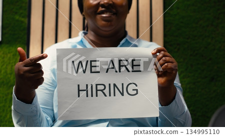African american female HR manager showing recruiting signs on papers to create a talent acquisition, announcing job vacancy and inviting skilled people to join the company workforce. 134995110