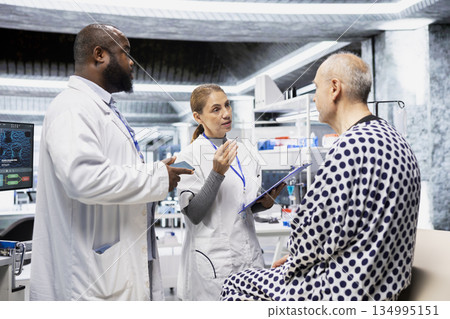 Team of experts monitoring senior patient vitals and DNA molecules on monitor, conducting a laboratory study and testing new treatment. Male doctor works on a medical breakthrough. 134995151