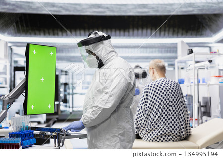 Vertical chroma key monitor next to scientist in protective gear examining virus symptoms of patient in prevention center. Safety data and breakthrough treatment results for bioscience. Vertical chroma key monitor next to scientist in protective gear examining virus symptoms of patient in prevention center. Safety data and breakthrough treatment results for bioscience. 134995194