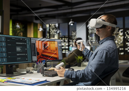 Male game developer using VR glasses and AI tech to design a spaceship for a video game, moving assets in 3D software for the spatial environment. Virtual development for the internet. Male game developer using VR glasses and AI tech to design a spaceship for a video game, moving assets in 3D software for the spatial environment. Virtual development for the internet. 134995216