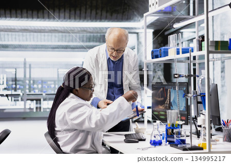 Diverse researchers in lab workspace conducting experiments and analyzing DNA tissue in jars. Biotechnology, genetics and chemistry tools highlight innovation in medicine. Molecular biology. Diverse researchers in lab workspace conducting experiments and analyzing DNA tissue in jars. Biotechnology, genetics and chemistry tools highlight innovation in medicine. Molecular biology. 134995217
