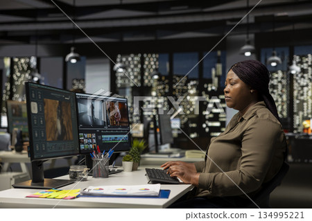 Female videographer editing a new music video on dual monitors in office, multitasking between montage editing and color grading. Professional editor uses tech tools and software. 134995221