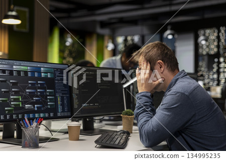 Dejected startup office engineer bummed by malfunctioning machine learning models enhancing automation. Sad Silicon Valley workplace IT expert concerned with broken AI assistant on computer 134995235