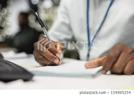 Close up of businessman extracting data and writing by hand from finance reports, drafting highlights for the company administration or management. Notetaking supports goal setting. Close up of businessman extracting data and writing by hand from finance reports, drafting highlights for the company administration or management. Notetaking supports goal setting. 134995254