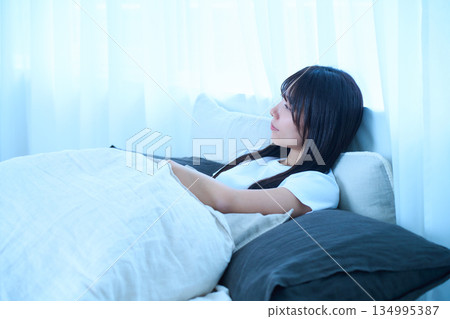 A young Japanese woman dozing in bed in the morning light. Lifestyle and health image. A young Japanese woman dozing in bed in the morning light. Lifestyle and health image. 134995387