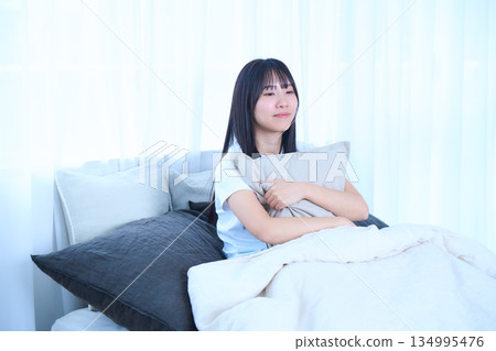 Young woman hugging a cushion in bed Young woman hugging a cushion in bed 134995476